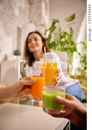 Hands clinking glasses with fresh juices in cozy interior. Hands clinking glasses with fresh juices in cozy interior. 135558444