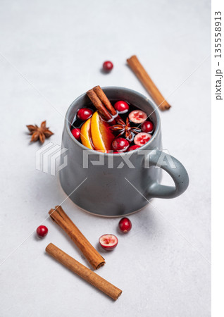 A cup of red mulled wine with cinnamon, orange and cranberry on a light background with spices. 135558913