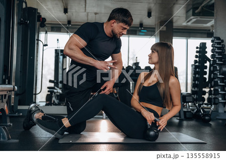 Trainer is helping. Man and woman are in the gym together Trainer is helping. Man and woman are in the gym together 135558915