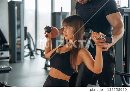 Helping with lifting dumbbells. Man and woman are in the gym together 135558920