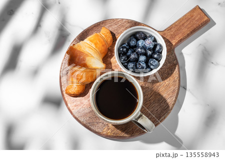 Freshly brewed espresso coffee in a cup, a croissant and blueberries on a wooden board 135558943