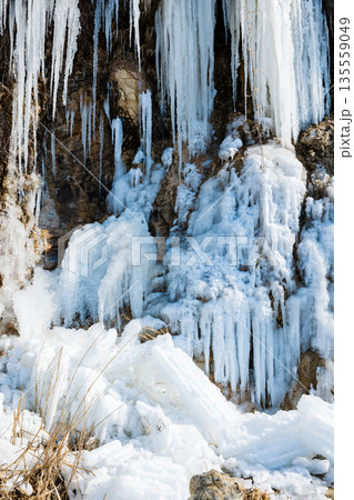 Stunning blue icicles hanging from a rocky cliff face by a frozen waterfall 135559049
