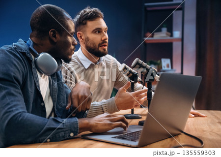 By the laptop. Two radio presenters recording an audio broadcast in a studio By the laptop. Two radio presenters recording an audio broadcast in a studio 135559303