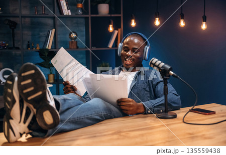 Reading from paper. Man is doing podcast in the studio Reading from paper. Man is doing podcast in the studio 135559438