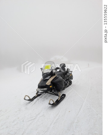 Snowmobile parked on foggy ski area near mountain lodge. Winter transport, resort logistics, and cold weather mobility through technology and alpine service operations. 135559622