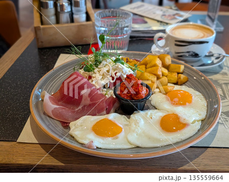 Hearty breakfast plate with eggs ham cheese and vegetables in cafe. Balanced meal choice, social dining, and modern breakfast culture in casual restaurant setting. Hearty breakfast plate with eggs ham cheese and vegetables in cafe. Balanced meal choice, social dining, and modern breakfast culture in casual restaurant setting. 135559664
