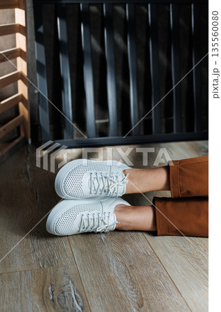 Close-up of female legs in white perforated leather sneakers. Women's summer sneakers. Collection of women's leather shoes Close-up of female legs in white perforated leather sneakers. Women's summer sneakers. Collection of women's leather shoes 135560080