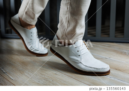 Male legs in leather summer shoes. Comfortable men's white moccasins without laces. Casual men's moccasins Male legs in leather summer shoes. Comfortable men's white moccasins without laces. Casual men's moccasins 135560143