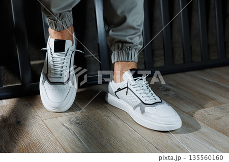 Casual white sneakers for men. Male legs in white leather summer shoes. Comfortable men's white sneakers with laces. Casual white sneakers for men. Male legs in white leather summer shoes. Comfortable men's white sneakers with laces. 135560160