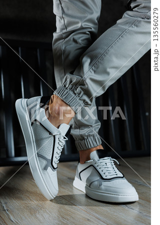 Male legs in white leather summer shoes. Comfortable men's white sneakers with laces. Casual men's sneakers 135560279