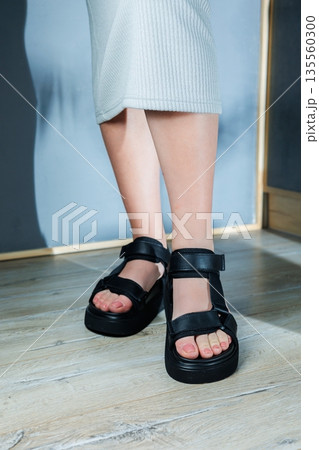 Black sports women's sandals on the feet. Stylish women's shoes for the summer. Collection of summer women's shoes. 135560300