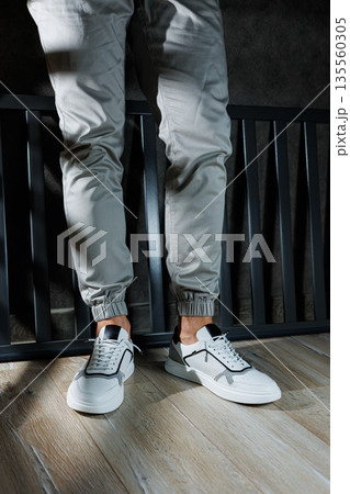 Male legs in white leather summer shoes. Comfortable men's white sneakers with laces. Casual men's sneakers 135560305