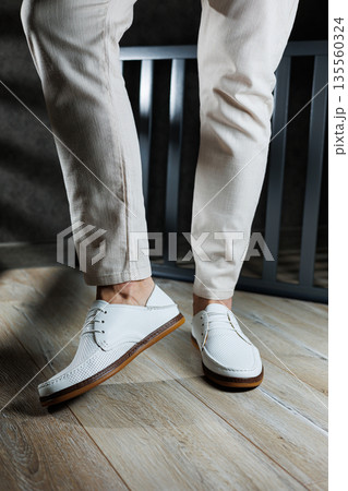 Male feet close-up in white casual shoes. Fashionable young man standing in leather stylish white moccasins in trousers. Seasonal summer men's shoes. Casual street style. Male feet close-up in white casual shoes. Fashionable young man standing in leather stylish white moccasins in trousers. Seasonal summer men's shoes. Casual street style. 135560324