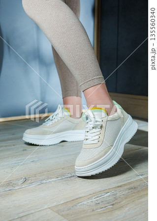 Close-up of female legs in leather sneakers on feet. Modern seasonal collection of stylish sneakers. Women's fashion. 135560340