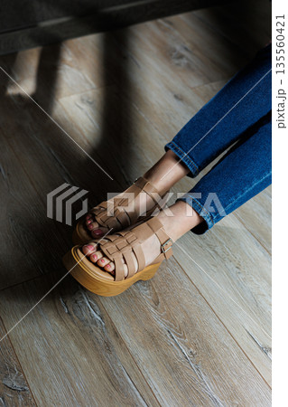 Beige leather sandals on women's feet. Female feet in comfortable casual sandals Beige leather sandals on women's feet. Female feet in comfortable casual sandals 135560421