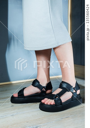 Black sports women's sandals on the feet. Stylish women's shoes for the summer. Collection of summer women's shoes. 135560424