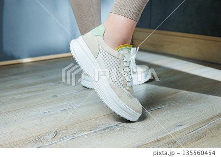 Close-up of female legs in leather sneakers on feet. Modern seasonal collection of stylish sneakers. Women's fashion. 135560454