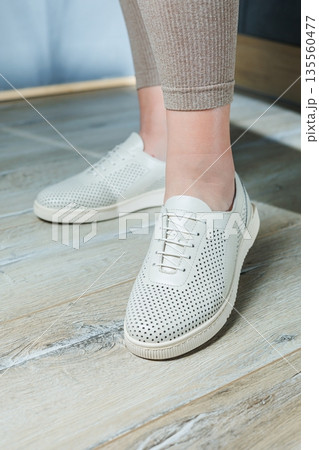Female legs in white casual sneakers. Comfortable women's summer shoes. Female legs in white casual sneakers. Comfortable women's summer shoes. 135560477