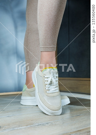 Close-up of female legs in leather sneakers on feet. Modern seasonal collection of stylish sneakers. Women's fashion. Close-up of female legs in leather sneakers on feet. Modern seasonal collection of stylish sneakers. Women's fashion. 135560480
