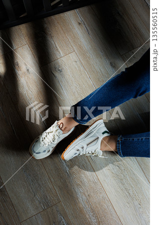 Female legs in white casual sneakers. Comfortable sports women's summer shoes. Female legs in white casual sneakers. Comfortable sports women's summer shoes. 135560515