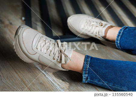 Collection of women's leather shoes. Female legs in leather beige casual sneakers. Stylish women's sneakers. 135560540