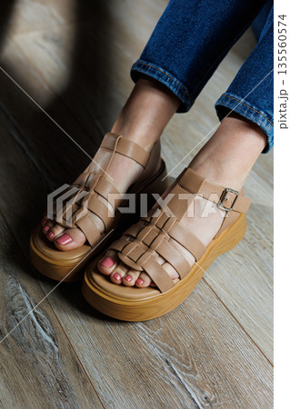 Beige leather sandals on women's feet. Female feet in comfortable casual sandals 135560574