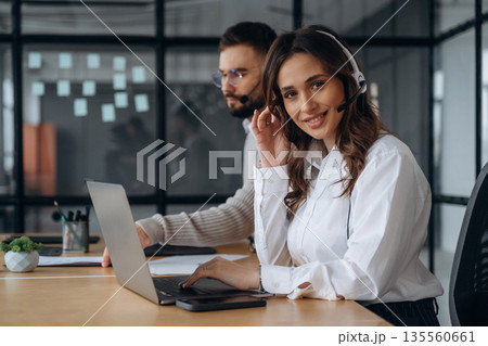 Support team in headphones. Man and woman are working in the office 135560661