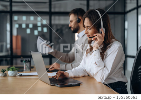 Support team in headphones. Man and woman are working in the office 135560663