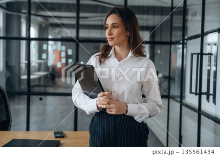 Notepad in hands. Beautiful woman is in the office 135561434