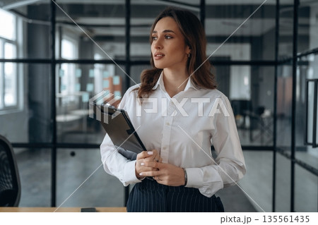 Notepad in hands. Beautiful woman is in the office 135561435