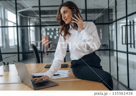 Talking by phone. Beautiful woman is in the office Talking by phone. Beautiful woman is in the office 135561439