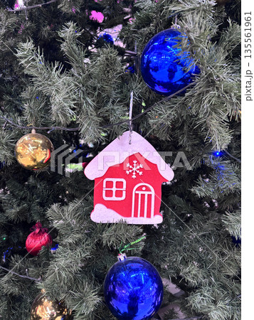 Colorful ornaments hang from a Christmas tree. Small house decorations are attached to the branches. Colorful ornaments hang from a Christmas tree. Small house decorations are attached to the branches. 135561961