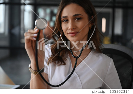 Cheerful, holding stethoscope. Woman doctor is in the office 135562314