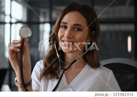 Cheerful, holding stethoscope. Woman doctor is in the office 135562315