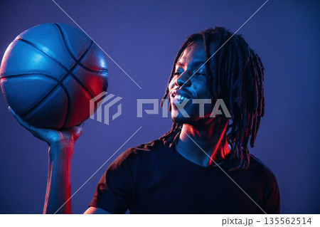 Dark room, basketball ball. African American guy is studio with neon lighting Dark room, basketball ball. African American guy is studio with neon lighting 135562514
