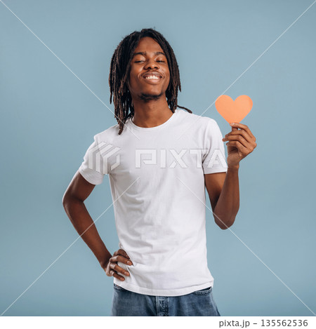 Paper heart, Valentine's day. Black man is in the studio against soft background Paper heart, Valentine's day. Black man is in the studio against soft background 135562536