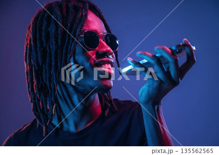 Stylish sunglasses, talking by phone. African American guy is studio with neon lighting 135562565