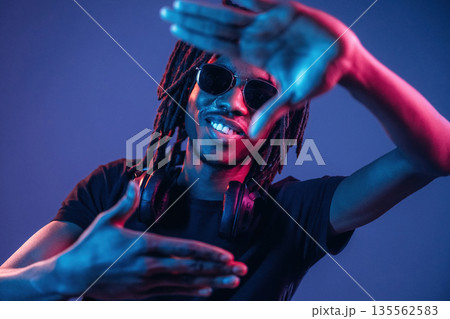 Gesture of capturing the photo. African American guy is studio with neon lighting Gesture of capturing the photo. African American guy is studio with neon lighting 135562583