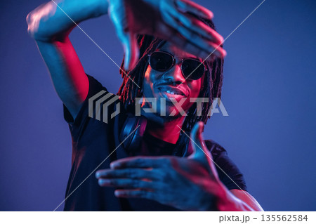 Gesture of capturing the photo. African American guy is studio with neon lighting 135562584
