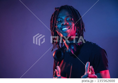 Friendly and cheerful facial expression. African American guy is studio with neon lighting 135562600