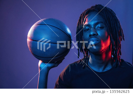 Showing basketball ball. African American guy is studio with neon lighting 135562625