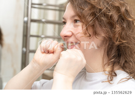 Woman performing oral care using dental floss, cleaning teeth and maintaining healthy gums in a bathroom 135562629
