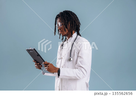 Holding notepad, doctor. Black man is in the studio against soft background Holding notepad, doctor. Black man is in the studio against soft background 135562656