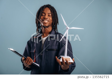 Green energy, wind turbine. Black man is in the studio against soft background Green energy, wind turbine. Black man is in the studio against soft background 135562715