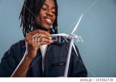 Green energy, wind turbine. Black man is in the studio against soft background Green energy, wind turbine. Black man is in the studio against soft background 135562716