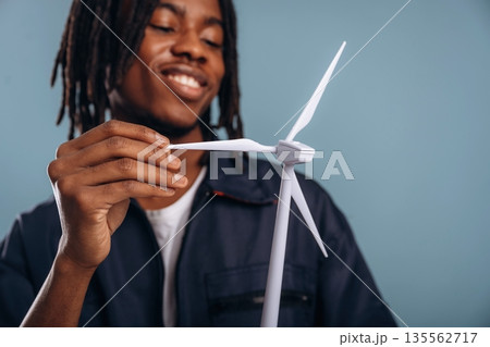 Green energy, wind turbine. Black man is in the studio against soft background Green energy, wind turbine. Black man is in the studio against soft background 135562717