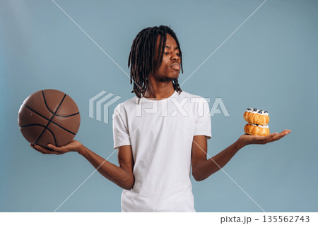 Choice between sweets and sport. Black man is in the studio against soft background Choice between sweets and sport. Black man is in the studio against soft background 135562743