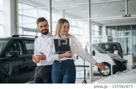 Black notepad in hands. Man and woman are in the car dealership 135562873