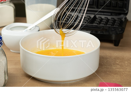 Hand Using a Whisk to Mix Raw Eggs in a White Bowl for Baking Waffles Hand Using a Whisk to Mix Raw Eggs in a White Bowl for Baking Waffles 135563077