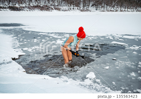 Senior woman breaking ice for winter swimming on frozen lake. Senior woman breaking ice for winter swimming on frozen lake. 135563423